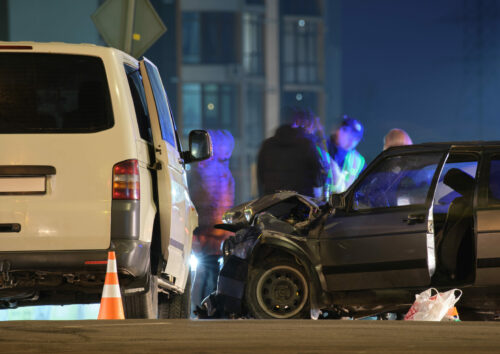 Cars crashed heavily in road accident after collision and silhouette of people on city street at night. Road safety and insurance concept