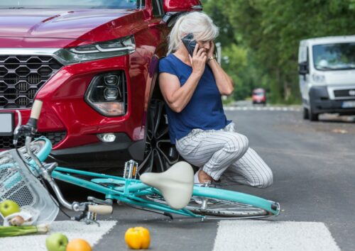 Senior woman leans against her red car and calls for help after causing an accident